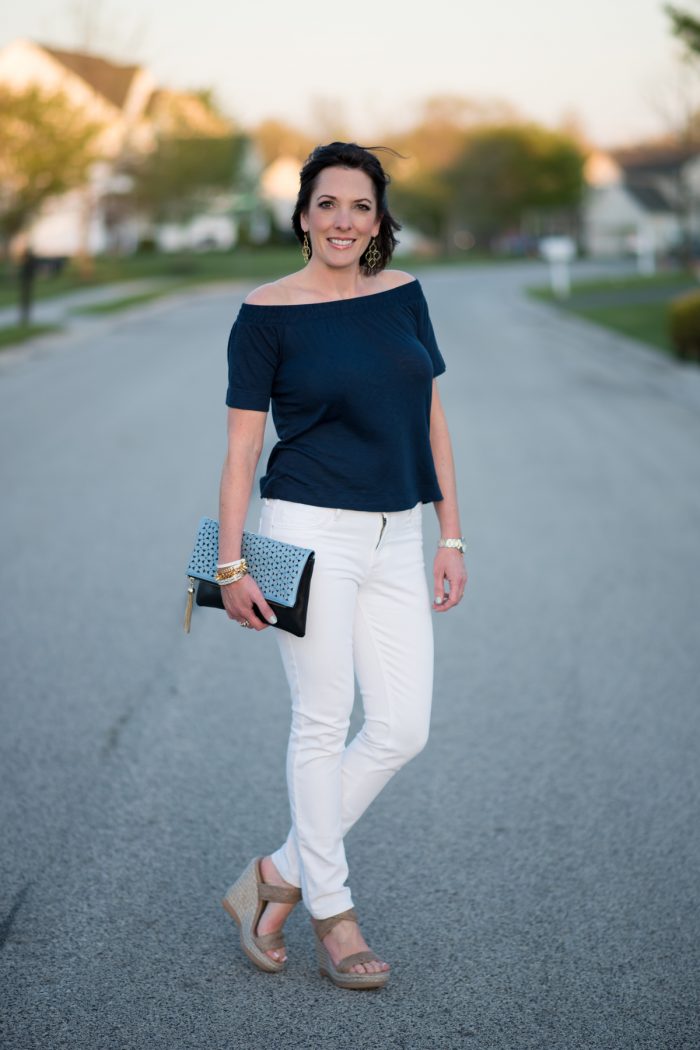 Jo-Lynne Shane styling a navy off the shoulder top with white jeans and wedge sandals. 